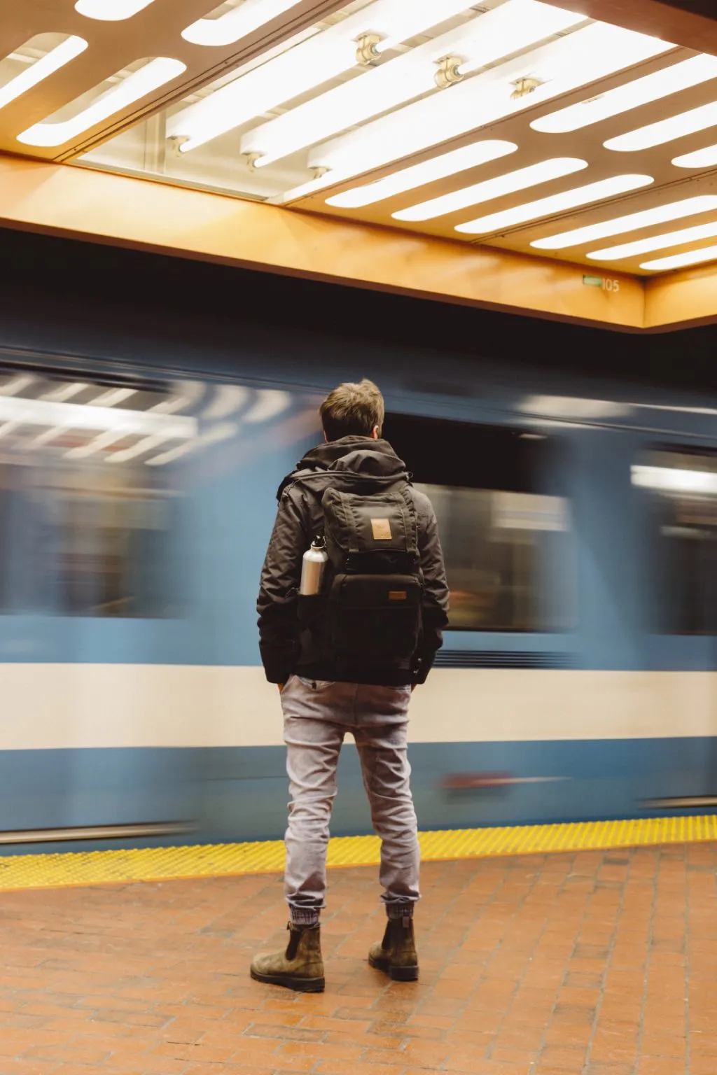 A waiting passenger seen from behind on a platform as a service passes